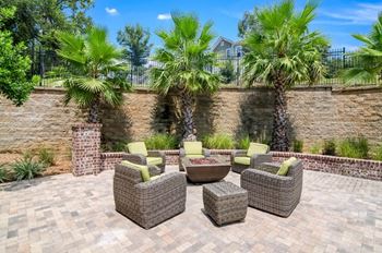 a patio with a fire pit and chairs in front of a brick wall
